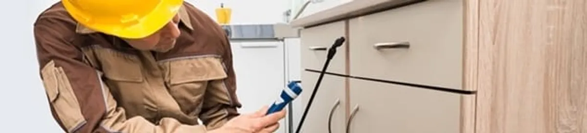 Roach exterminator applying treatment under kitchen cabinets in San Diego, CA